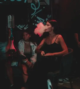 A guest enjoying a relaxing shisha session in a dimly lit, atmospheric lounge, perfectly capturing the vibe of where to smoke & buy Tombacco in Bali.