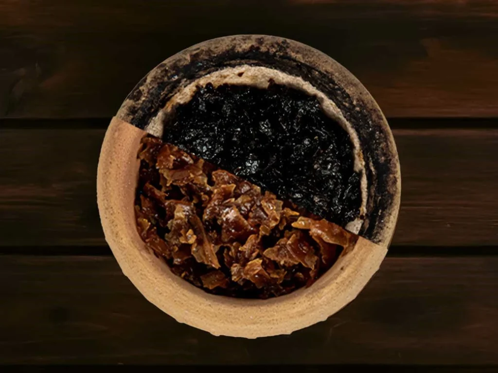 A close-up looking directly down into a clay hookah bowl packed half with dark burley and half with light virginia leaves, serving as a great visual reference for the base materials used whether you prefer herbal or tobacco shisha.